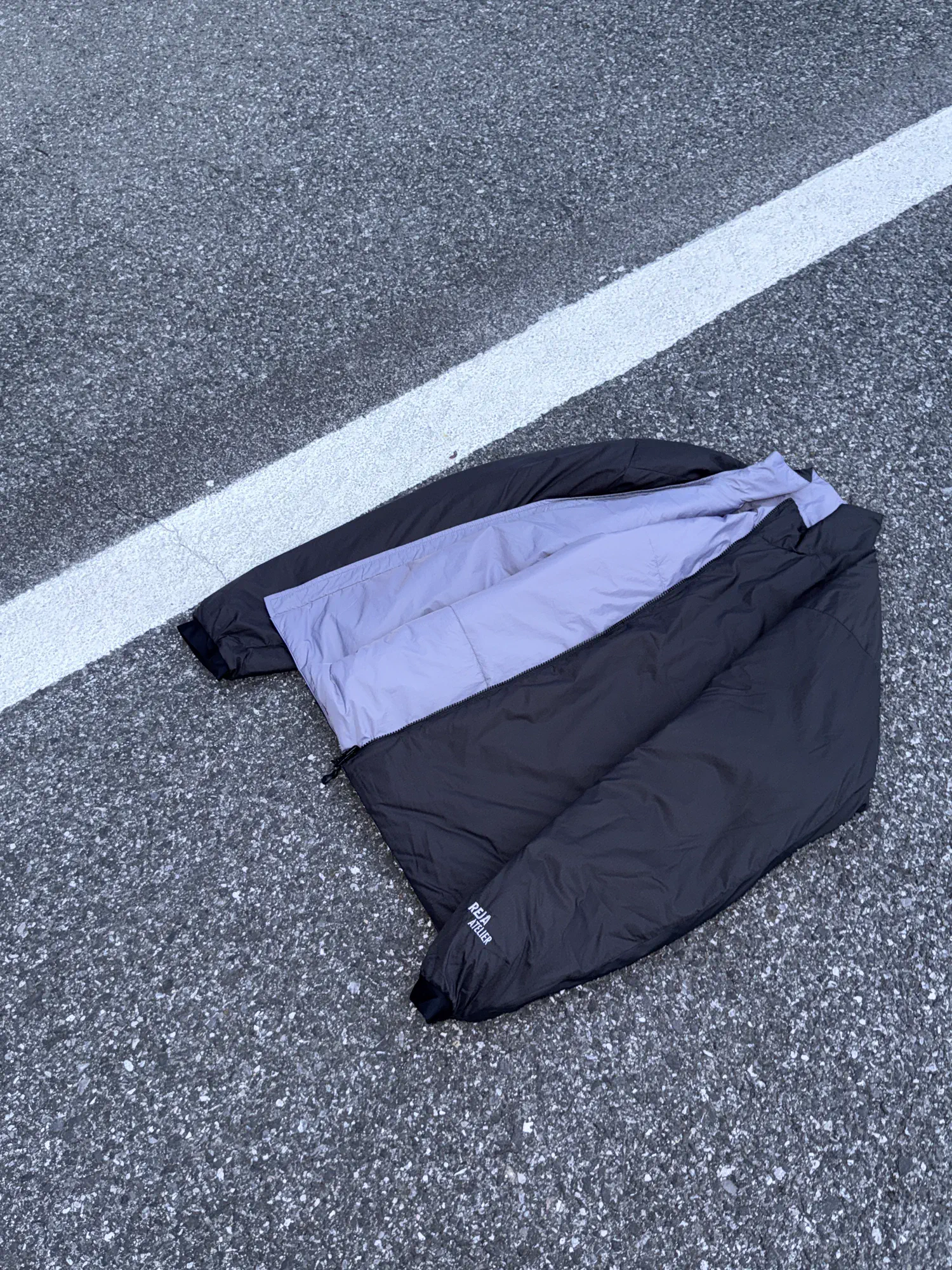 黑色与淡紫色双面 REJA 夹克平铺于道路